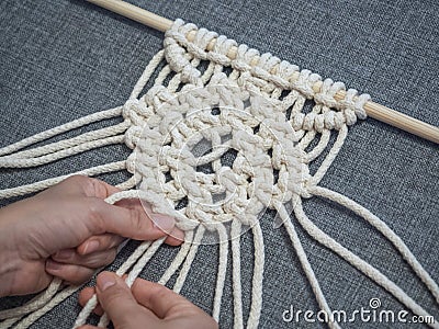 Macrame. Girl weaves macrame. White thread, female hand, grey background, close-up Stock Photo