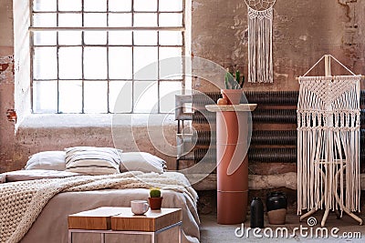 Macrame in a wabi sabi bedroom interior with a bed, table and stand with a plant Stock Photo