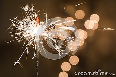 Burning sparkler stands in a glass. Dark background with defocused multi-colored lights of garland. Stock Photo