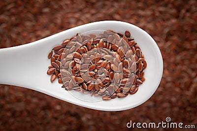 Macro Close up of Organic Brown flaxseeds Linum usitatissimum or linseed on a white ceramic soup spoon in a blurred background. Stock Photo