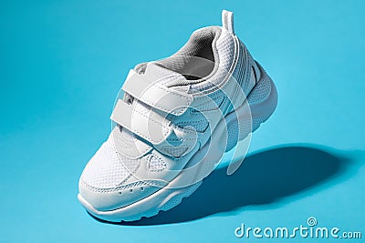 macro flying white child sneakers with velcro fasteners isolated on a blue background with hard light Stock Photo