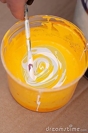macro hand mixes yellow and white paint with a wooden stick in a plastic container Stock Photo