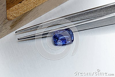 Macro mineral faceted stone sapphire with tweezers on a gray background Stock Photo