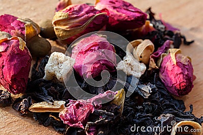 Macro photo of tea with a tea rose. The composition of the heap of tea roses and dried hibiscus flower located on a wooden Board. Stock Photo
