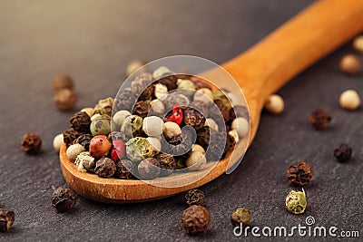 Extreme close up a of peppercorn mix in a wooden spoon on a dark stone kitchen board Stock Photo