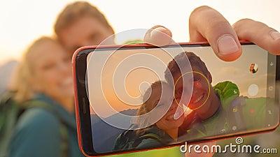 MACRO: Smiling young hiker couple taking a selfie on mountaintop at sunrise. Stock Photo