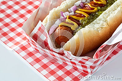 Macro view of a hotdog in a checkered tray topped with mustard, ketchup and relish, ready for eating. Stock Photo
