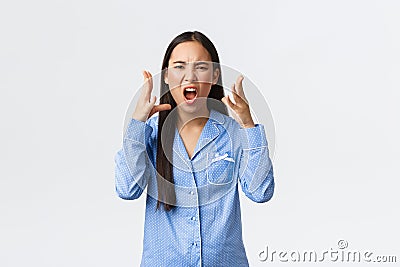 Mad outraged asian girl in blue pajamas arguing, having argument with girlfriend during sleepover, swearing or cursing Stock Photo