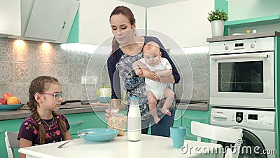 Madre con el bebé que cocina el desayuno sano para una más vieja hija almacen de video Madre con el bebé que cocina el desayuno sano para una más vieja hija almacen de video