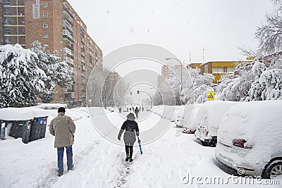 MADRID, SPAIN - JANUARY 9, 2021. Sheltered people walking on the snow-filled road. Editorial Stock Photo