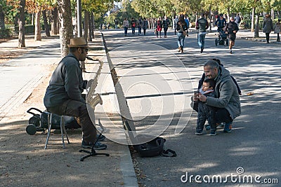 Madrid, Spain - November 12,2017 : Unidentified father and child watch a street performer play the saxophone in Retiro Park Madrid Editorial Stock Photo
