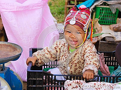 MAE SALONG, THAILAND - DECEMBER 17. 2017: Portrait of a happy toddler baby from Akha hill tribe in a shopping box on market with Editorial Stock Photo
