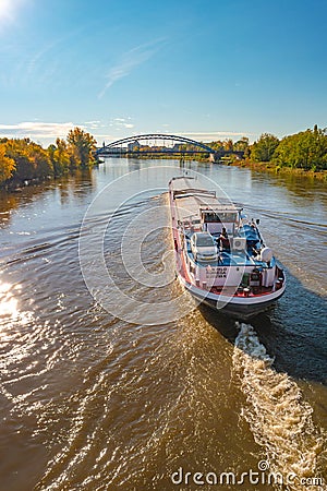 Magdeburg historical downtown, Elbe river, modern arch Sterne Bridge with coming a big cargo ship with a car, barge, in golden Editorial Stock Photo