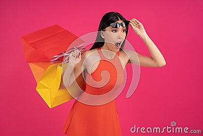 Mage of a beautiful shocked young asian woman posing isolated over pink wall background holding shopping bags. dressed in orange Stock Photo