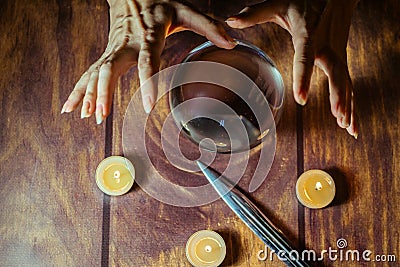 Magic crystall ball, knife, candles and hands of the foreteller or the witch making manipulations on the ball Editorial Stock Photo