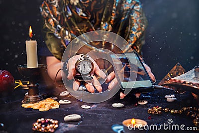 Magic and online fortune telling. The witch is holding a watch on a chain and a smartphone. Close up Stock Photo