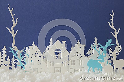 Magical Christmas paper cut winter background landscape with houses, trees, deer and snow in front of blue background. Stock Photo