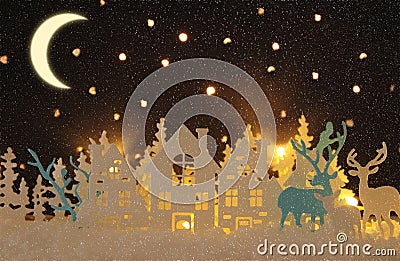 Magical Christmas paper cut winter background landscape with houses, trees, deer and snow in front of night starry sky background. Stock Photo