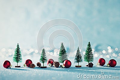 Magical miniature winter wonderland background. Evergreen trees, pine cones and red christmas baubles on shiny blue background. Stock Photo