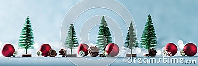 Magical miniature winter wonderland banner. Evergreen trees, pine cones and red christmas baubles on shiny blue background. Stock Photo