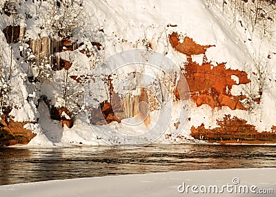 Magical sunny winter day, landscape with red sandstone cliffs that are snowy with snow, frozen icicles on the cliff wall Stock Photo