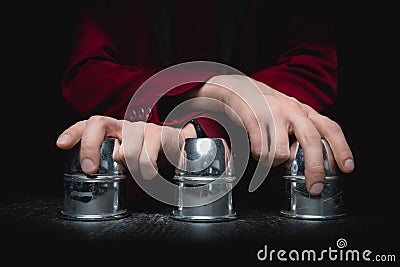 Magician shows shell game of thimbles with circles and ball, black background. Concept deception, sleight hand Stock Photo