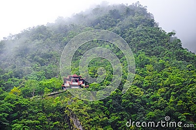 Magnificent Chinese temple on a steep rock surrounded by green tropical forest. Misty weather, fog. Taiwanese landscape, travel Stock Photo