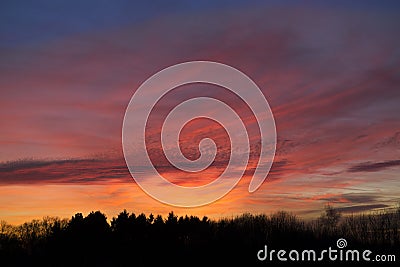 Magnificent evening sky with colorful orange and red clouds over silhouette of a forest in backlight. Stock Photo