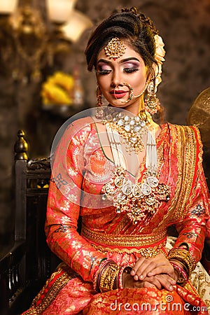 Magnificent young Indian bride in luxurious bridal costume with makeup and heavy jewellery is sitting in a chair Stock Photo