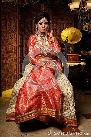 Magnificent young Indian bride in luxurious dress and precious jewellery is sitting in a chair in a luxury apartment. Classic Stock Photo