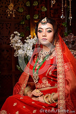 Magnificent young Indian bride in luxurious dress and precious jewellery is sitting in a chair in a luxury apartment. Classic Stock Photo