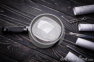 Magnifier, compasses and rolls from the drawing on a black wooden background Stock Photo