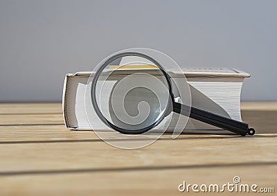 Magnifying glass with close thick book on wood table with day light Stock Photo