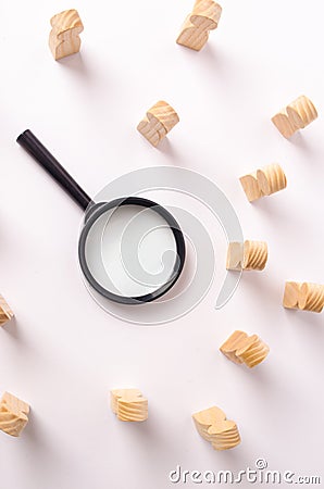 A magnifying glass lies in the center of the wooden figures of people who look at it. The concept of the search for workers Stock Photo