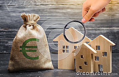 Magnifying glass is looking at a bag with euro money and three houses. Affordable cheap loan, mortgage. Taxes, rental income. Stock Photo