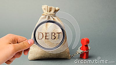 A magnifying glass is looking at a money bag with the word Debt and a borrower is bound by handcuffs. Mandatory payment of debt. Stock Photo