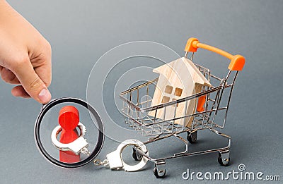 Magnifying glass is looking at a person is handcuffed to a house on a supermarket cart. Financial dependence, unavailable housing Stock Photo