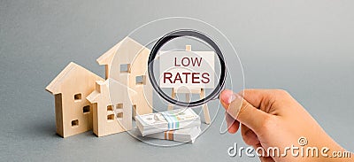 A magnifying glass is looking at a poster with the word Low rates and wooden house. The concept of reducing interest rates on Stock Photo