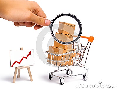 Magnifying glass is looking at the Supermarket cart with boxes and a graph with red arrow, merchandise: the concept of buying Stock Photo