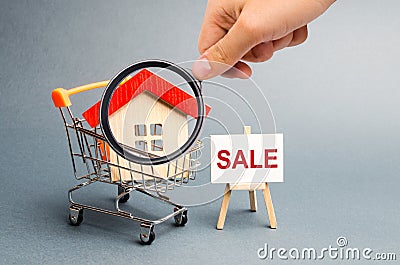 Magnifying glass is looking at the Supermarket cart with houses and a Sale Poster. The concept of selling a home, real estate Stock Photo