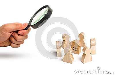 Magnifying glass is looking at the Wooden figurines of people stand around the house. Search for a new home and real estate. Stock Photo