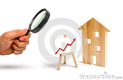 Magnifying glass is looking at the Wooden house stand with red arrow up. Growing demand for housing and real estate. Stock Photo