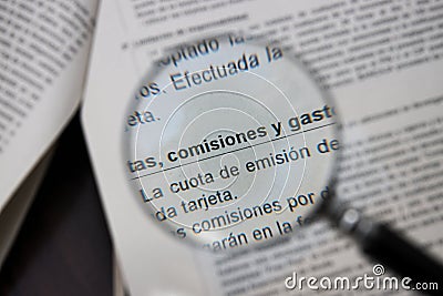 A magnifying glass points to the Spanish words commissions, fees and expenses on a bank document Stock Photo