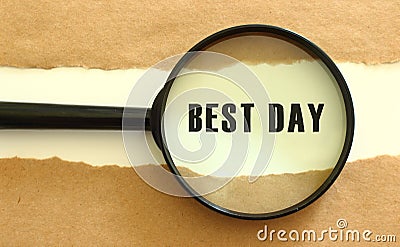 The magnifying glass reveals the BEST DAY text appearing behind the torn brown paper. Stock Photo