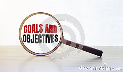 Magnifying glass with text GOALS AND OBJECTIVES on wooden table Stock Photo