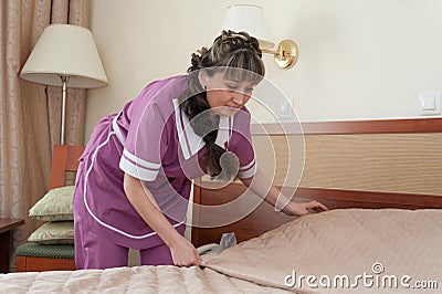 Maid girl, dressed in purple, putting blanket on bed Editorial Stock Photo