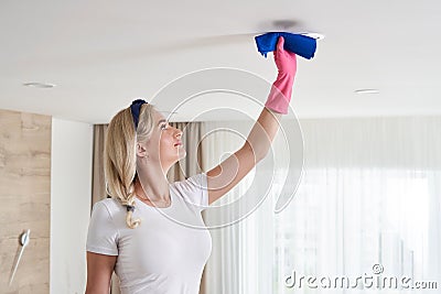 Maid woman holding mop pile, cleaning ceiling in living room. House cleaning service concept. Stock Photo