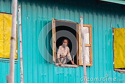 Maing Thauk, Myanmar - April 2019: old Burmese woman looking out of the floating house window Editorial Stock Photo