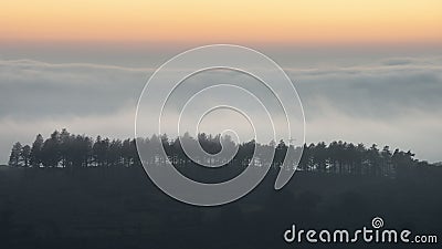 Majestic landscape image of cloud inversion at sunset over Dartmoor National Park in Engand with cloud rolling through forest on Stock Photo