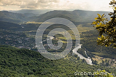 Majestic mountain landscape with green valley, river, village, lush green forest on ridges of slopes in summer sunny day with gold Stock Photo